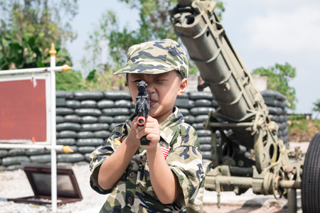 Young boy dressed like a soldier with a gun in barracksの写真素材