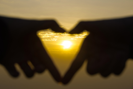Hands in shape of Heart around sunsetの写真素材