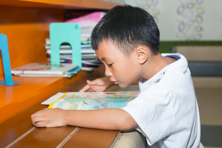 Cute little boy reading book in the libraryの写真素材