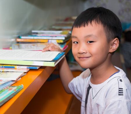 Cute little boy reading book in the libraryの写真素材