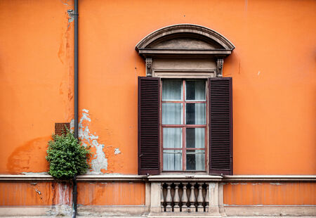 Window and shutter of Italian house on bright colored orange wall.