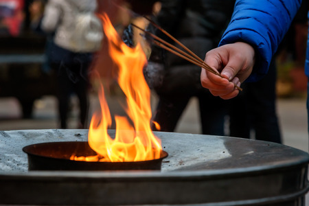 Lighting incense stick by fire inside the chinese temple.の写真素材