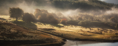 Looking over the valley as patches of light appear and disappear across the foggy landscape of Peak...