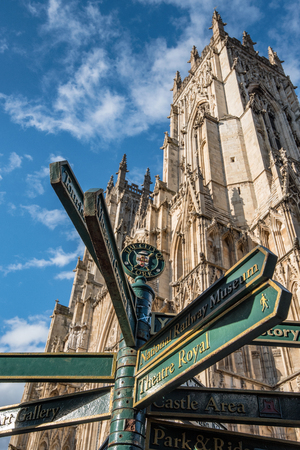 York Minster tower with a background of blue sky and a sign board showing different directions,...