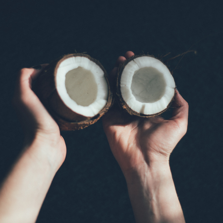 Girl holding half of a coconut isolated darkの写真素材