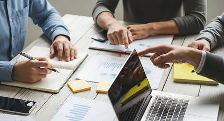 Three people collaborating around a wooden table with laptop and documents business meetingの素材