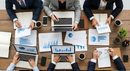 Overhead view of business people collaborating around a wooden table with laptops and charts meeting 1の素材