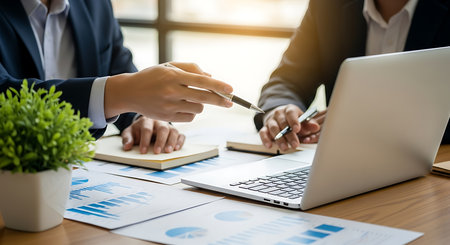 Two business people discussing charts and laptop on wooden desk meeting discussionの素材