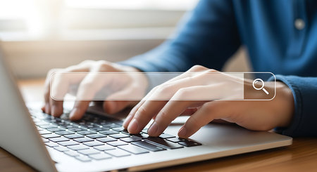 Close up of hands typing on a laptop keyboard with a transparent search bar overlay and magnifying glass icon.の素材