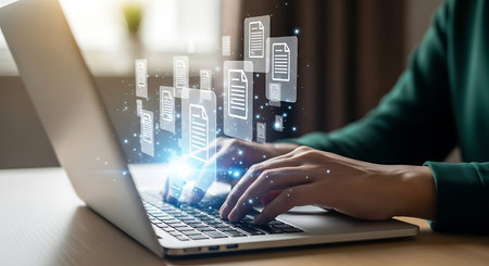 Hands typing on a laptop keyboard with glowing digital document icons floating above. Blue light and particles emanate from the screen.の素材