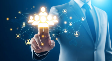 A man in a suit touches a glowing network of interconnected human icons against a dark blue background with a subtle world map.の素材