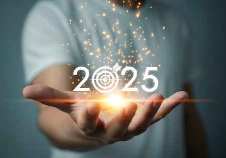 A hand holds the glowing numbers 2025, with the zero replaced by a target symbol. Orange light and golden sparkles emanate from the digits.の素材