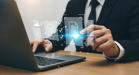 A businessman in a dark suit interacts with a glowing digital interface displaying document icons and checklists, with a laptop in the foreground.の素材