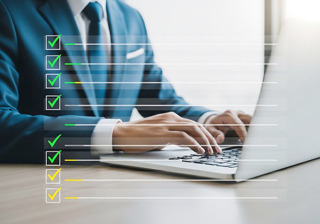 A person in a blue suit types on a laptop, with a digital checklist showing green and yellow checkmarks and progress bars overlaid.の素材