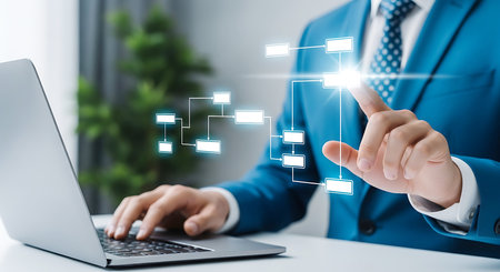 A man in a blue suit touches a glowing digital flowchart projected in front of him while using a laptop.の素材