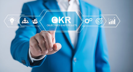 A person in a blue suit touches a digital interface displaying OKR objectives and key results with icons for ideas, teamwork, gears, targets, and growth charts.の素材