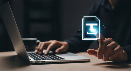 A person's hands are visible, one typing on a laptop keyboard and the other touching a glowing blue and white download icon on a dark background.の素材