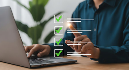 A person in a blue shirt uses a laptop, with a digital checklist showing green checkmarks and lines on the screen.の素材