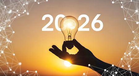 A silhouette of a hand holds a glowing lightbulb containing a brain graphic against a warm sunset sky with the year 2026 superimposed.の素材