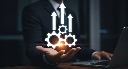 White gears and upward arrows hover over a man's open palm, with a laptop in the foreground.の素材