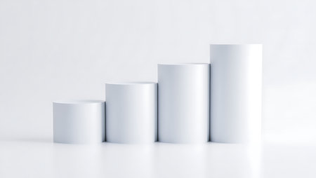 Four white cylindrical pedestals of increasing height stand on a reflective white surface against a plain white background.の素材