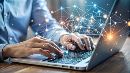 Close-up of hands typing on a laptop with a glowing blue and orange network overlay.の素材