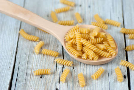 Italian uncooked fusilli pasta in wooden spoon on old wooden tableの写真素材