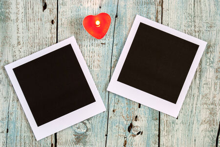 Instant photo frames and heart shaped candle on old wooden table