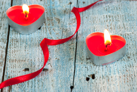 Two heart shaped candles and red ribbon on old wooden tableの写真素材