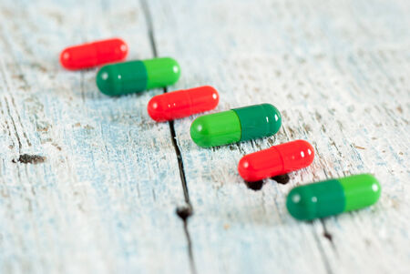 Green and red pills on old wooden tableの写真素材