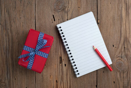 Notebook with gift box and red pencil on old wooden backgroundの写真素材