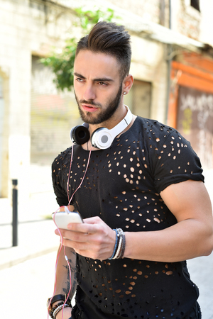 Young man using smartphone with headphones around his neck outdoorの写真素材