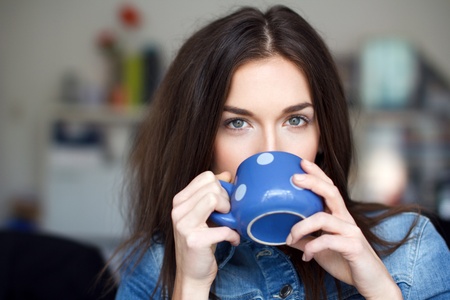 Young brunette woman with dotted blue mug drinking coffeeの写真素材