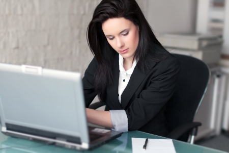 Businesswoman typing on laptop, indoor office, blank paper with penの写真素材