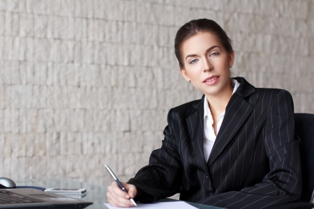 Businesswoman writing letter with pen on desk in officeの写真素材