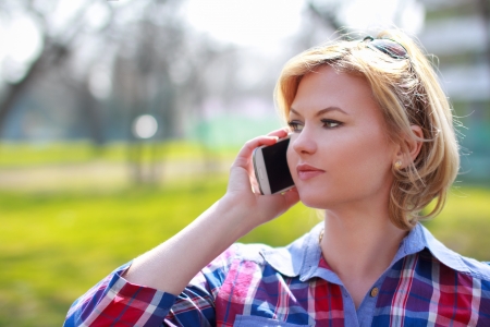Attractive blonde woman calling with smartphone at parkの写真素材