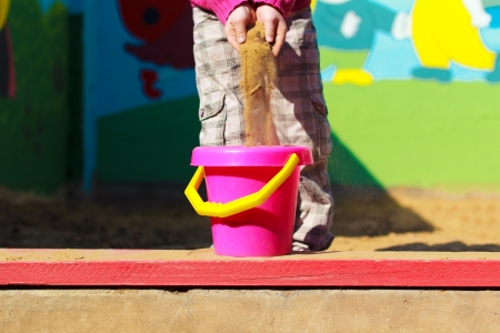 Cute girl scattering sand in the pink bucketの写真素材