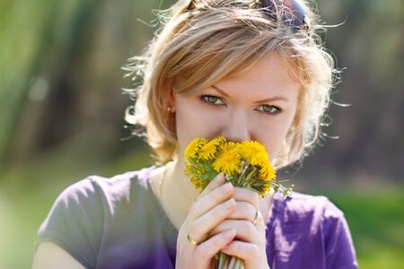 Young blonde woman smell dandelion yellow flowerの写真素材