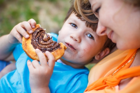 Cute boy eating chocolate snail with motherの写真素材