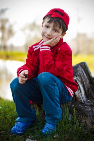 Cute child in red cap sitting on trunk at riverの写真素材