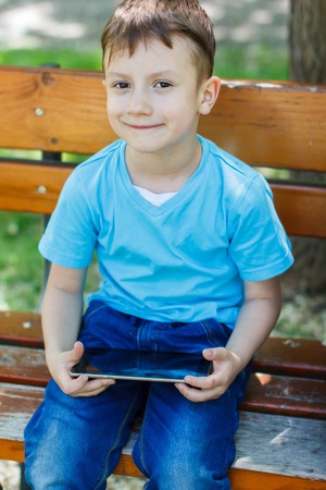 Happy boy sitting on bench with tabletの写真素材