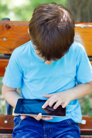 Little boy sitting on bench with tablet, parkの写真素材
