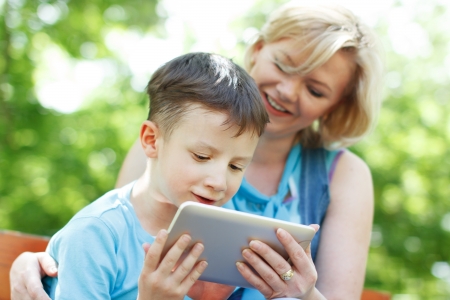 Happy mother and son with tablet sitting on bench, outdoorsの写真素材