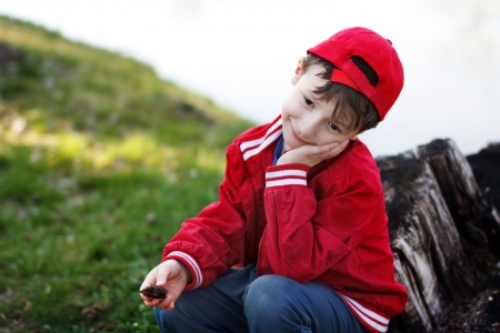 Little boy sitting in red cap on trunk at river, childhoodの写真素材