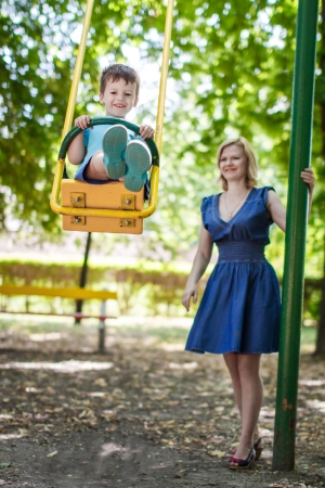 Little son swinging in park with motherの写真素材