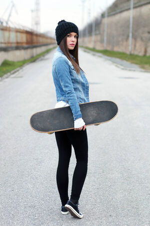Woman holding skateboard, looking backの写真素材