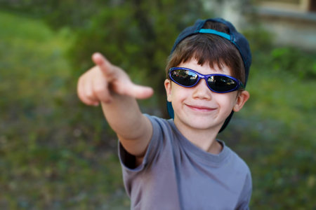 Little boy in blue cap and sunglasses pointing the sky