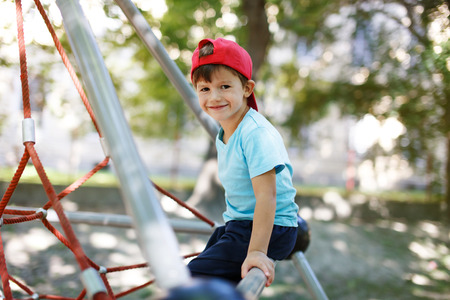 Little boy in cap sit on jungle gym, outdoor portrait