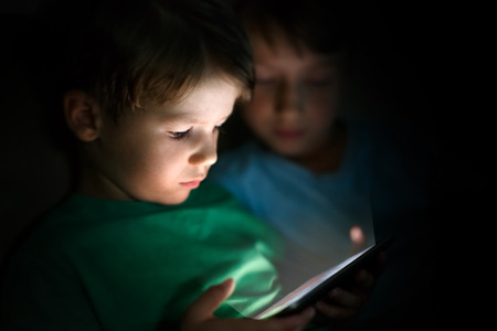 Little brothers playing on tablet at nightの写真素材