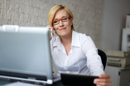 Blonde businesswoman in glasses call by smartphone in officeの写真素材